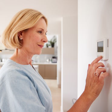 Woman changing temperature on thermostat to conserve energy
