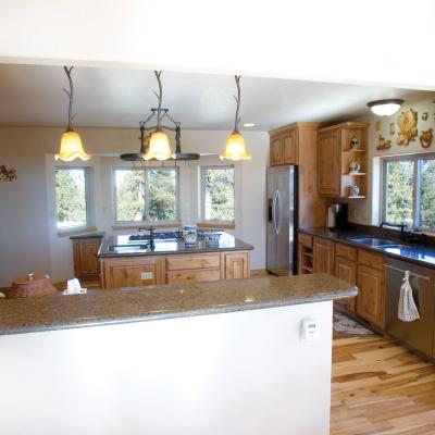 Looking into kitchen with natural hardwood floors, black granite counter and large island with cooktop stove